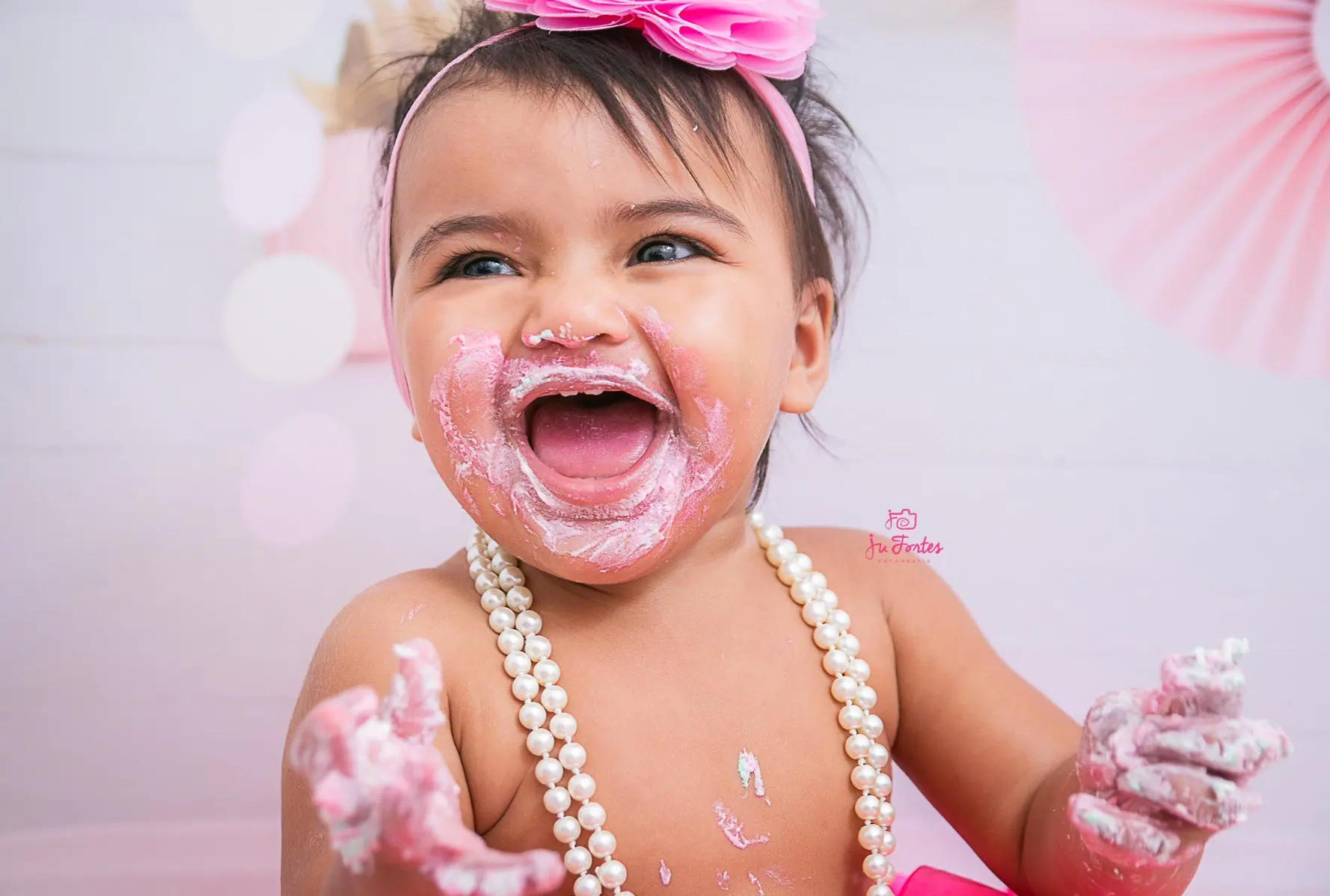 Bebê sorrindo com o rosto sujo de bolo em ensaio smash the cake rosa