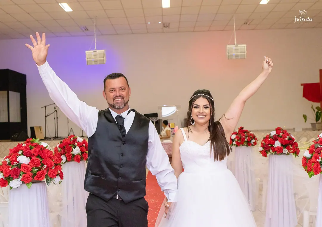 Noivos comemorando com os braços para cima no salão da festa de casamento