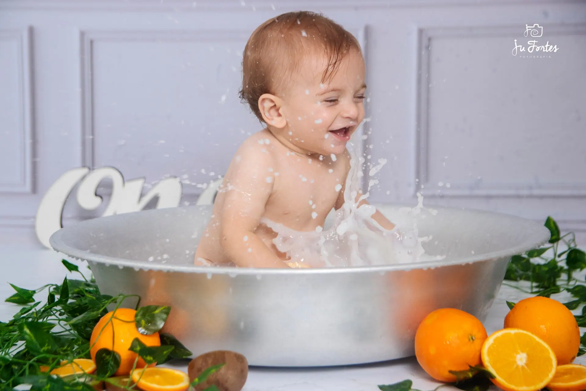 Bebê brincando na banheira em ensaio com laranjas e folhagens