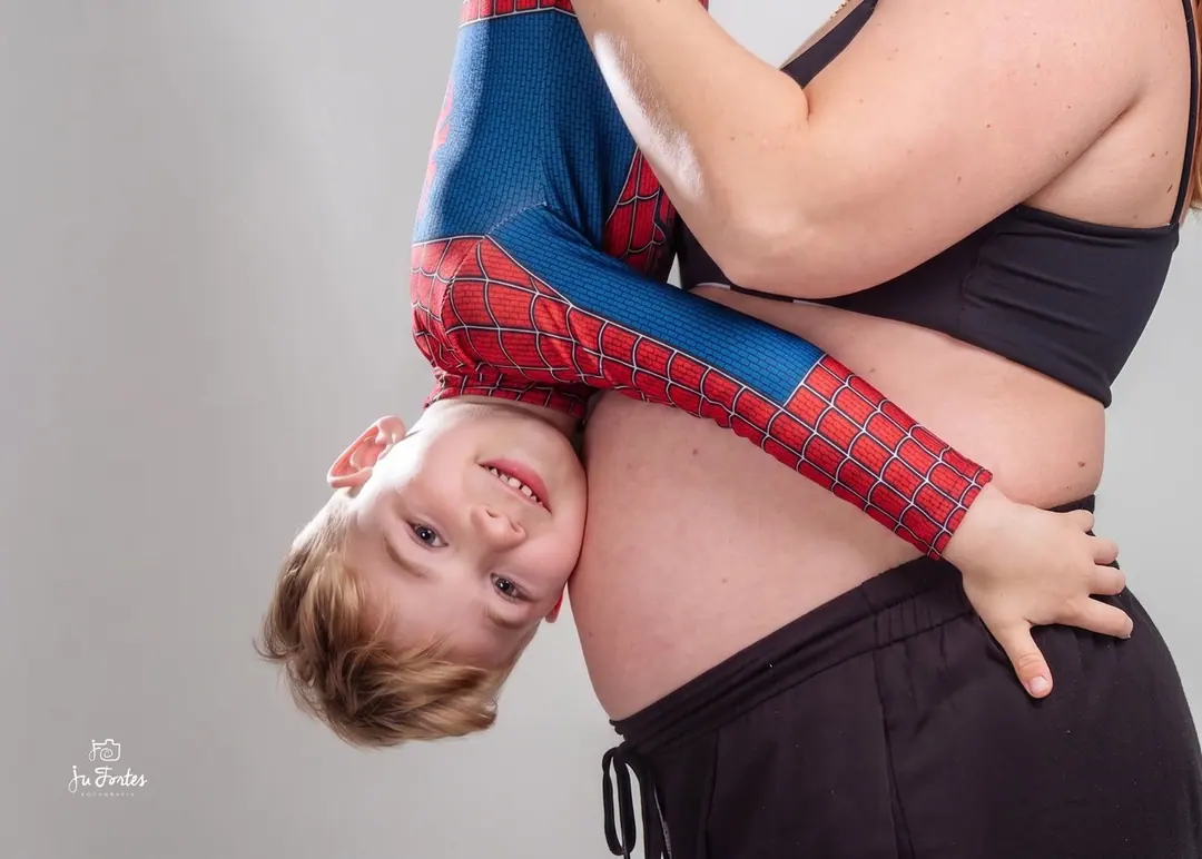 Menino fantasiado de herói abraçando a barriga da mãe gestante