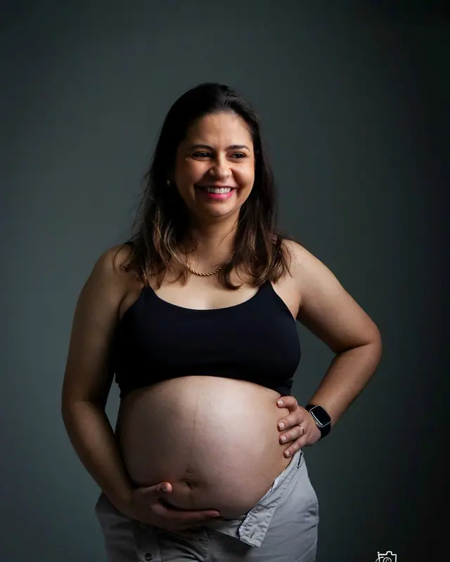 Gestante sorrindo com a mão na barriga em ensaio de estúdio