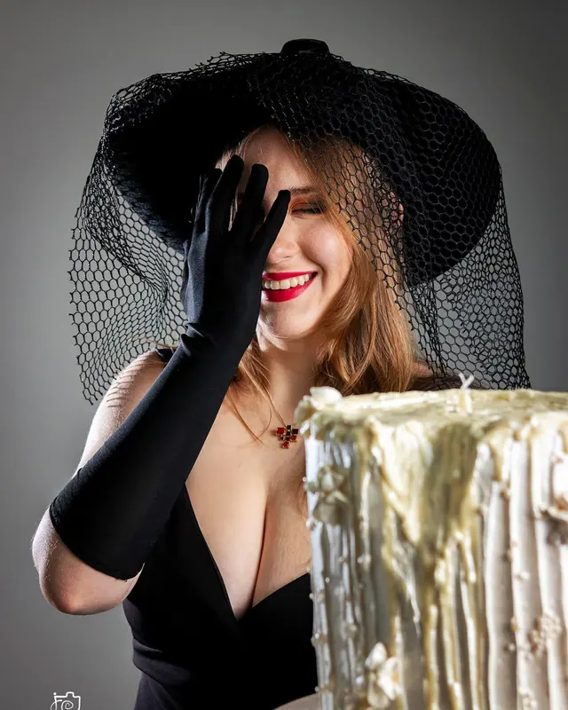 Mulher de chapéu e luvas pretas rindo em ensaio smash the cake adulto
