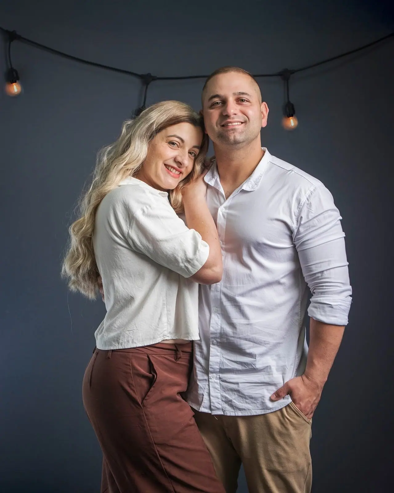 Casal abraçado em ensaio de estúdio com varal de luzes